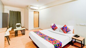 Una habitación de hotel con cama, escritorio, silla, mesita de noche y ventilador de techo.