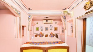 A pink-themed bedroom with a double bed, decorative pillows, a ceiling fan, and wall-mounted air conditioning unit. - Fabhotel Khandaka Mahal (Jaipur)