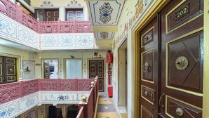 A multi-level building with ornate balconies, decorative ceilings, and a central corridor leading to a large wooden door marked with the number 202. - Fabhotel Khandaka Mahal (Jaipur)