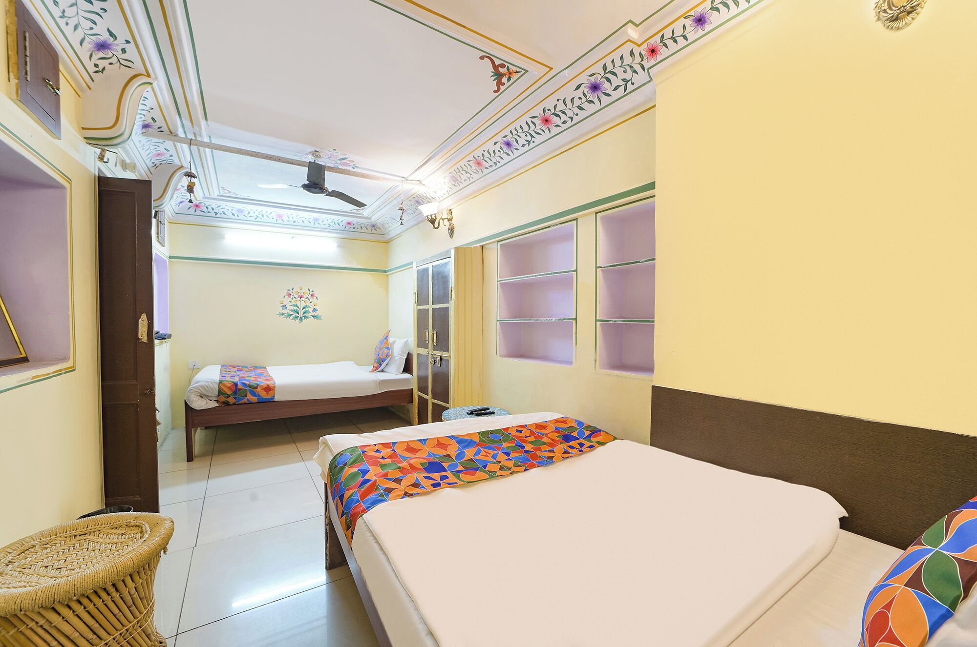 Habitación de hotel con dos camas, ventilador de techo, paneles decorativos en la pared y suelo de baldosas.