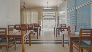 Un salón de conferencias con varias mesas y sillas de madera, ventanas amplias y un ventilador de techo.