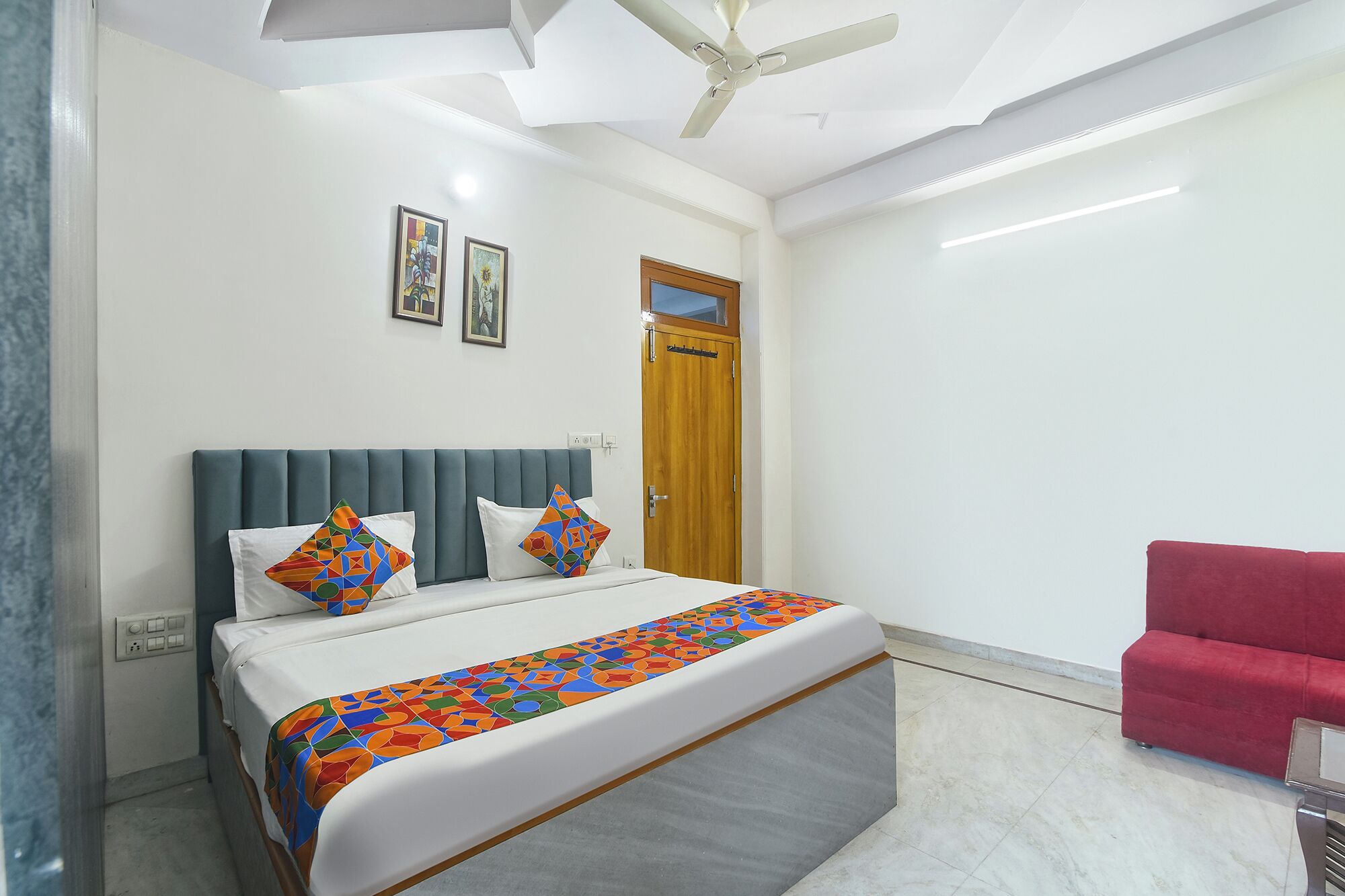 A bedroom with a bed, a ceiling fan, a door, and a red chair.