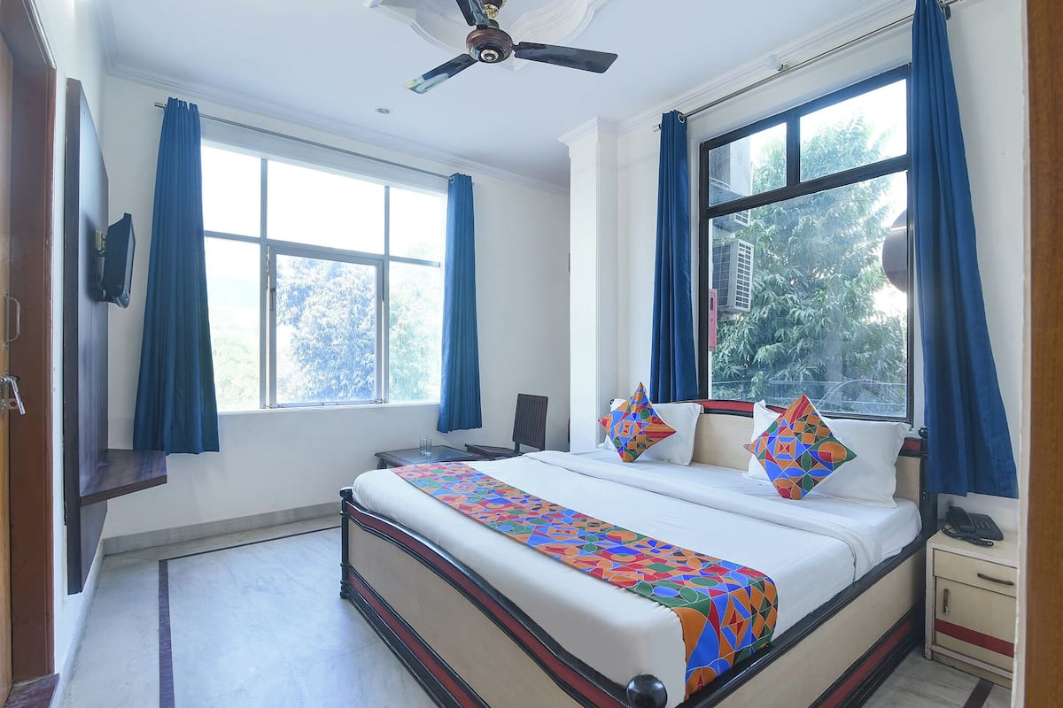 A hotel room with a large bed, two windows with curtains, a ceiling fan, and a bedside table with a phone.