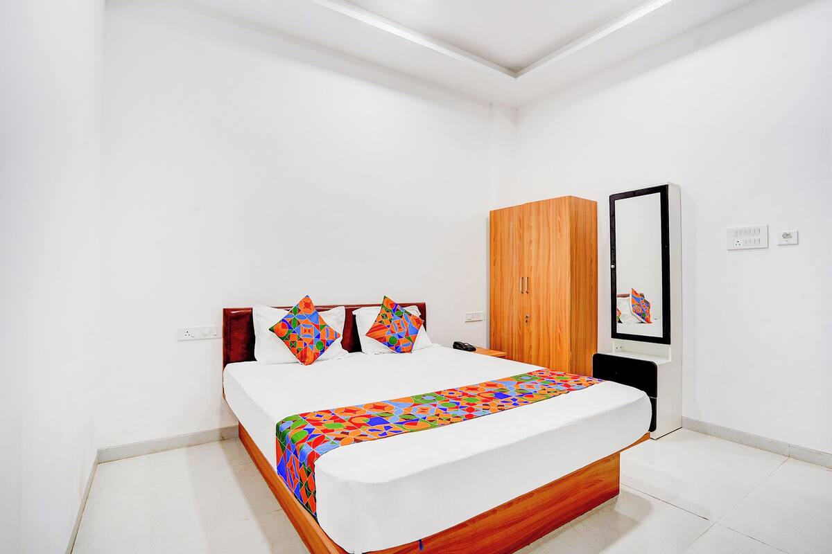 A bedroom with a bed, a wooden wardrobe, a mirror, and a bedside table.