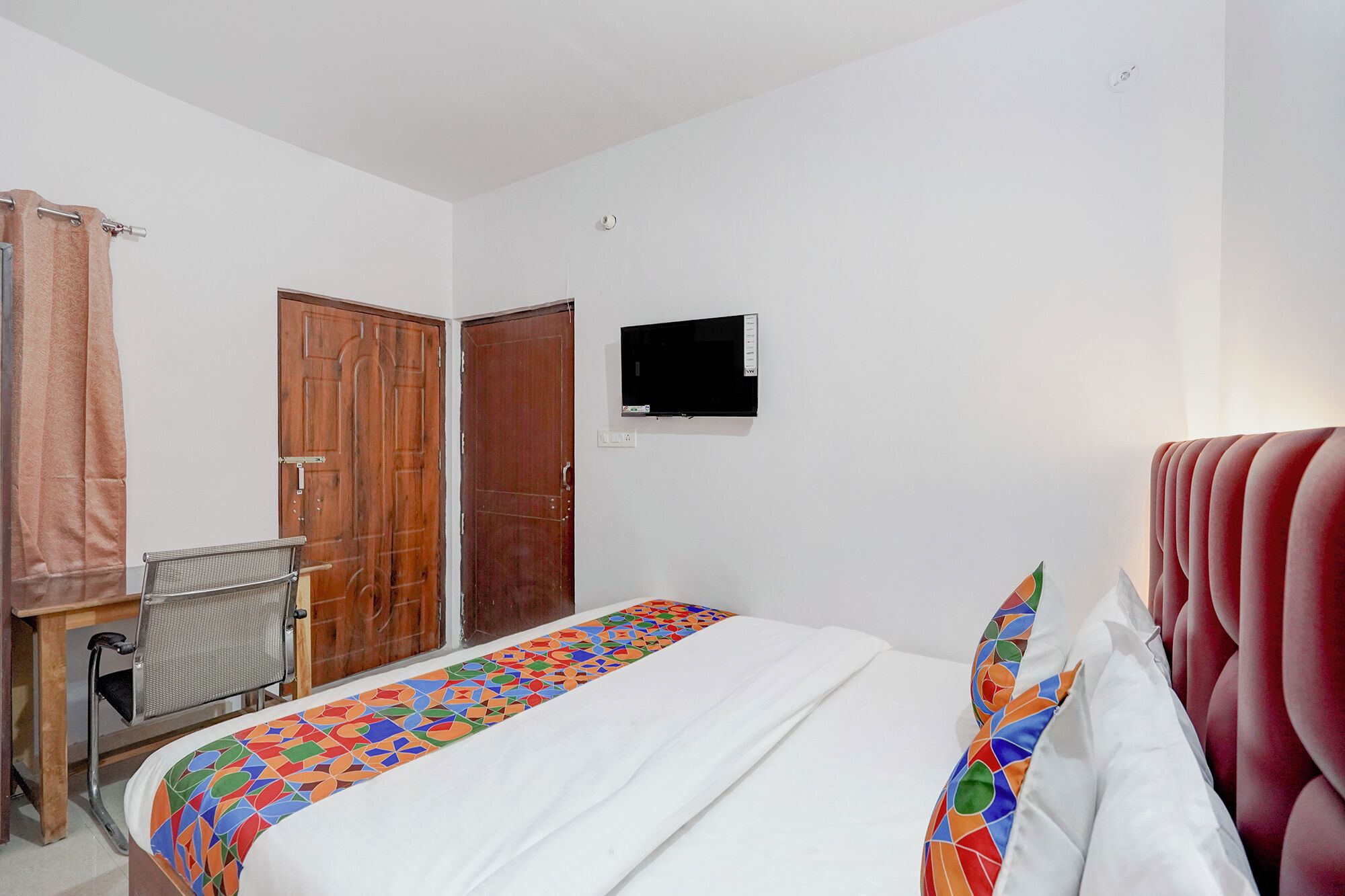 A hotel room with a bed, a desk, a chair, and a TV mounted on the wall.