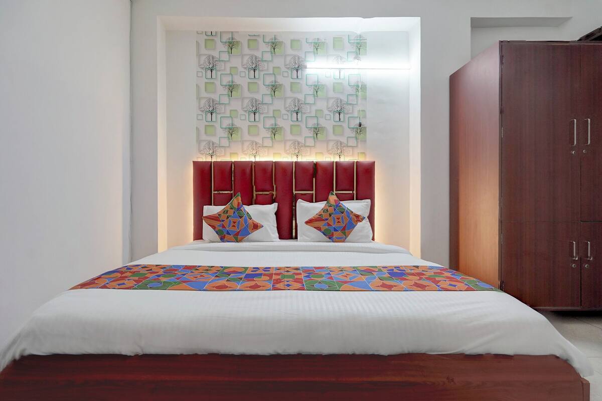 A bed with a geometric patterned bedspread, a red upholstered headboard, and two decorative pillows.