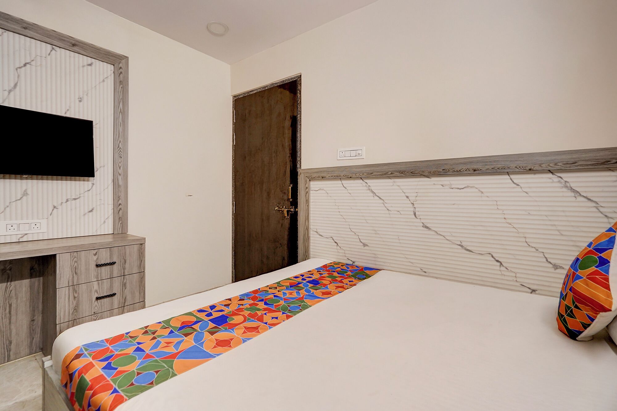A bedroom with a bed, a TV mounted on a wooden cabinet, and a door.