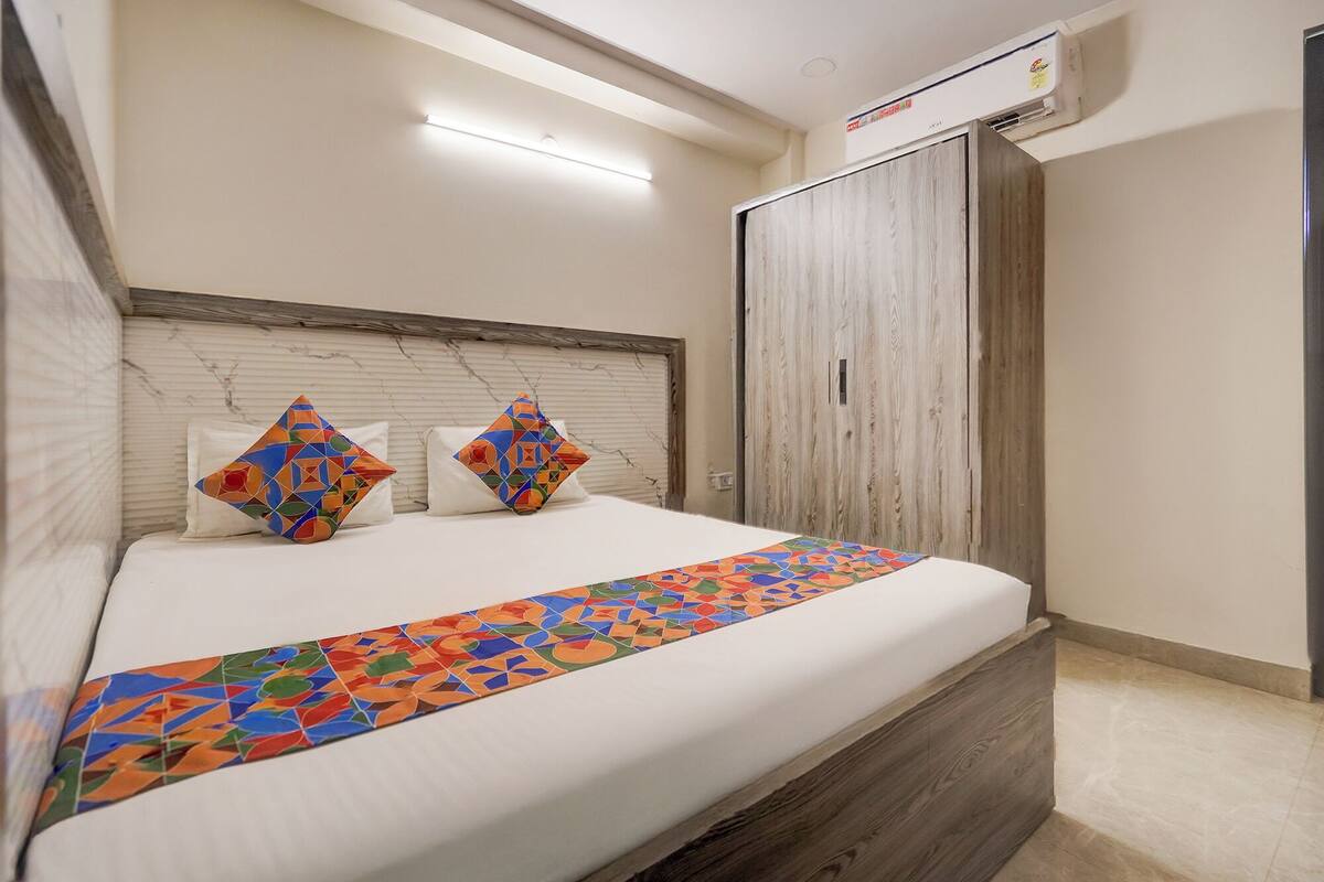 A neatly made bed with a colorful geometric-patterned bed runner, two pillows with a similar pattern, a wooden headboard, and a wardrobe with a light wood finish.