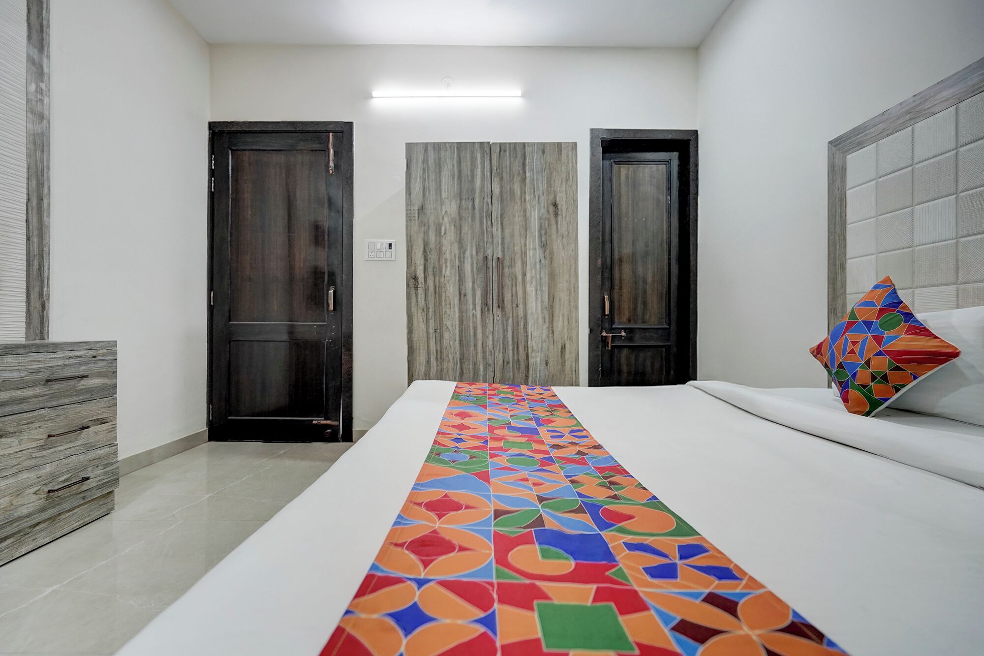 Quarto de hotel com uma cama grande, uma cômoda de madeira e duas portas.