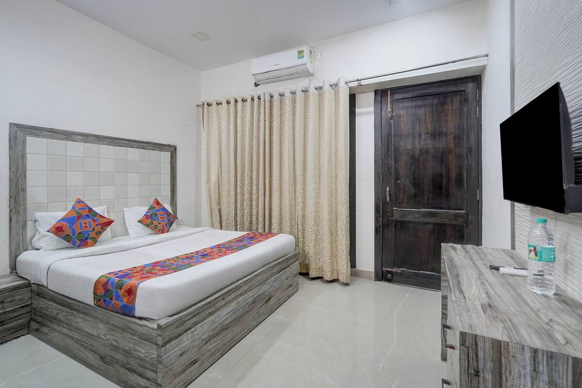 A hotel room with a bed, a wooden nightstand, a TV, a desk, and a door.