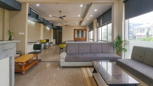 A modern living room with a grey sofa, a wooden coffee table, and a small dining area with yellow chairs. - Via Reyansh (Jaipur)