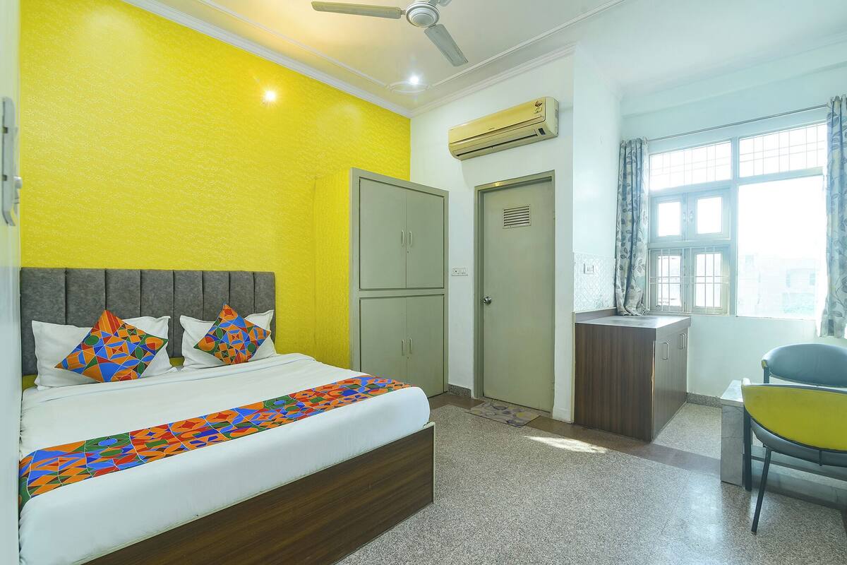 A hotel room with a bed, a desk, an air conditioning unit, a window with curtains, and a ceiling fan.