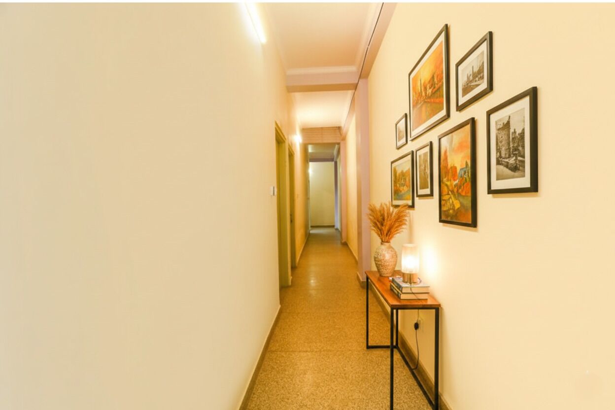 A hallway with a polished floor, a wall adorned with framed pictures, and a small table with a vase and a lamp.
