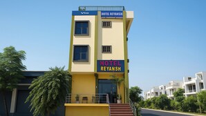 A multi-story hotel named 'Hotel Reyansh' with a yellow facade, a visible staircase, and a clear sky. - Via Reyansh (Jaipur)