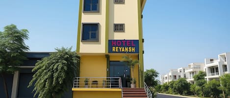 A multi-story hotel named 'Hotel Reyansh' with a yellow facade, a visible staircase, and a clear sky.