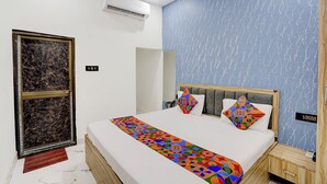 A hotel room with a bed, a nightstand, a wooden wardrobe, a wall-mounted air conditioner, and a door with a marble-patterned frame. - Fabhotel Vrrinda Residency (Varanasi)