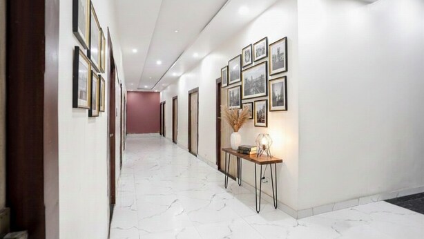 A hallway with framed pictures on the walls, a marble floor, and a small table with a vase and books. - Fabhotel Vrrinda Residency (Varanasi)