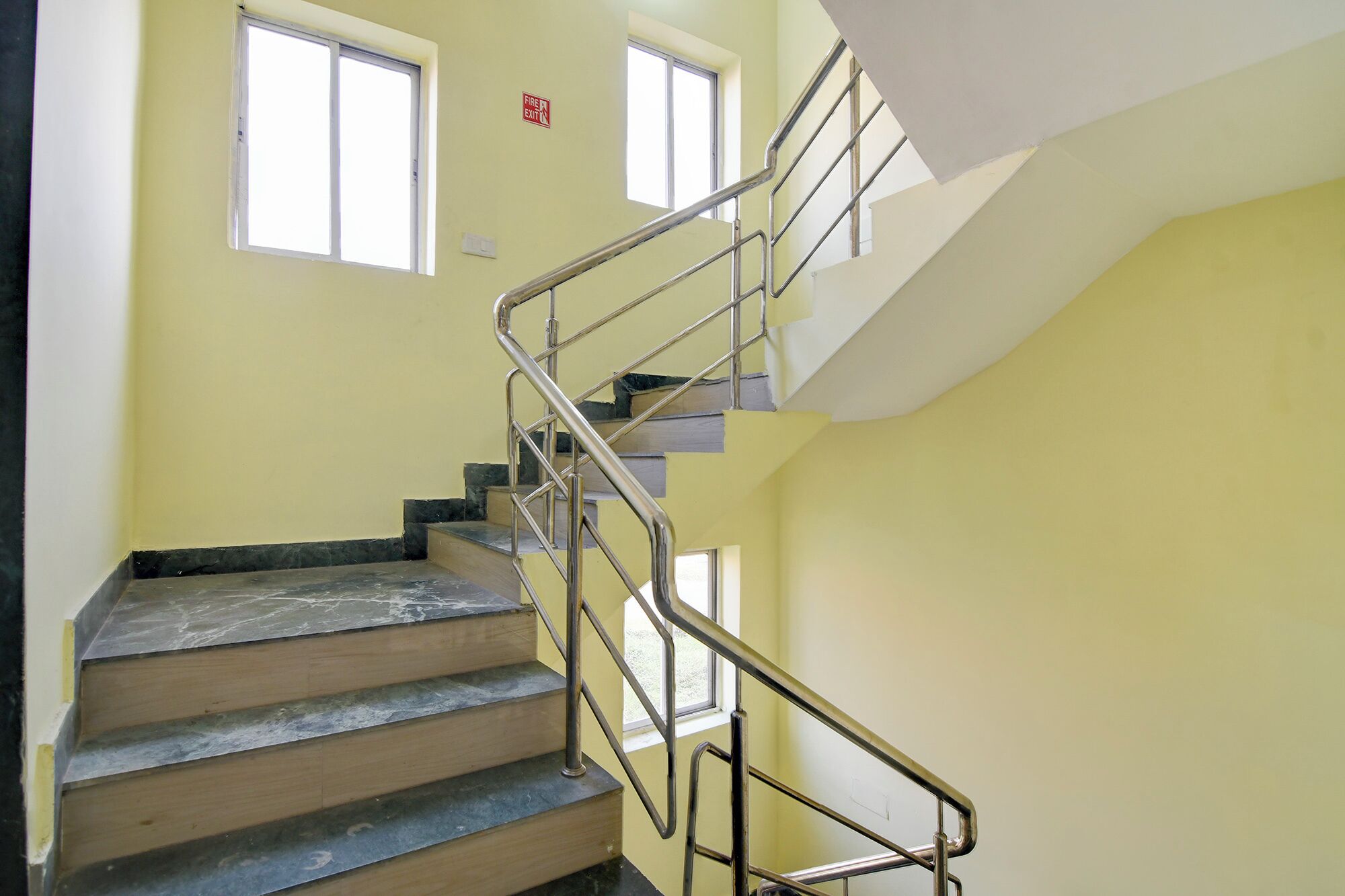 Eine Treppe mit Metallgeländern, einem Brandschutztürschild und zwei Fenstern.