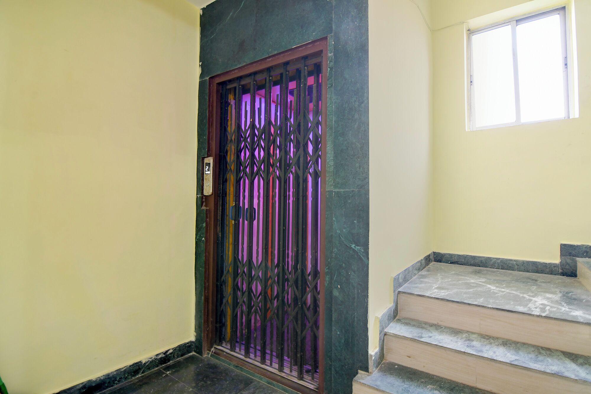 A door with a metal gate, a small window, and a set of stairs leading to an upper floor.