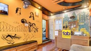 Un hall d’hôtel comprenant un comptoir d’accueil, un espace détente avec un canapé et un banc en bois, ainsi qu’un mur orné de peintures murales artistiques.