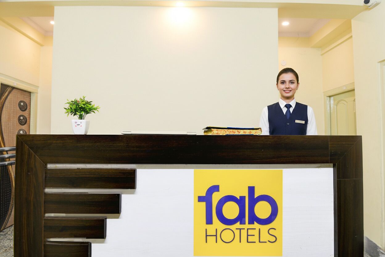 A reception desk with a sign reading "fab hotels" and a plant on the left.