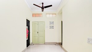 Un pasillo con ventilador de techo, una puerta verde y un enchufe en la pared.