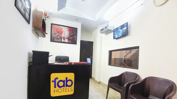 Un comptoir d’accueil avec une enseigne indiquant « fab hotels », un tableau représentant une vue sur la ville et deux chaises en plastique.