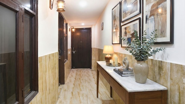 Un pasillo con suelo de mármol, paneles de madera, un escritorio con un jarrón, obras de arte enmarcadas y una puerta al final.