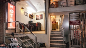Zona de recepción de un hotel con una escalera que conduce a un piso superior, un mostrador de recepción y un cartel que indica que el personal de entrega no está autorizado a entrar.