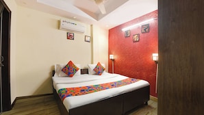 Una habitación de hotel con cama, ventilador de techo, equipo de aire acondicionado, pared roja y suelo de madera.