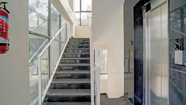 Una scala con ringhiere in vetro che conduce a un piano superiore, un estintore sulla parete e una porta con pannello di sicurezza.