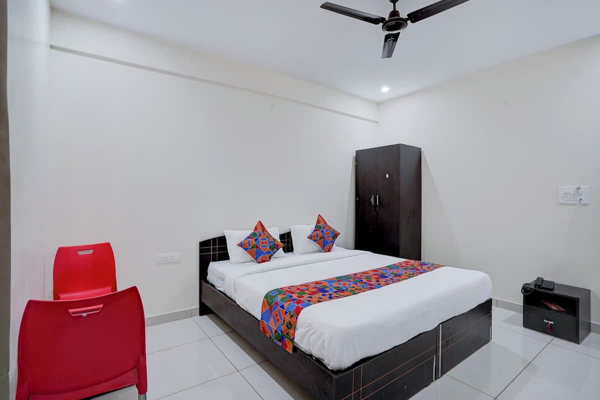 A bedroom with a bed, a red chair, a wardrobe, and a ceiling fan.