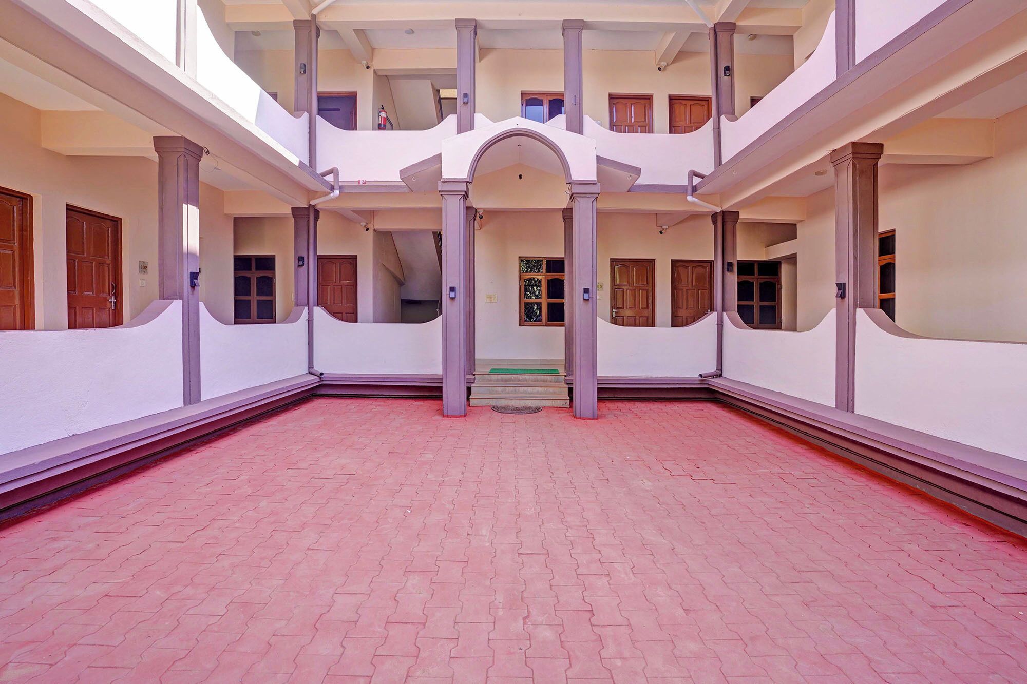 A spacious courtyard with a central archway, surrounded by balconies and wooden doors.