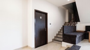 A modern interior with a dark wooden door, a staircase with a dark grey cushioned landing, and a marble floor. - Fabhotel Paradise Inn (Indore)