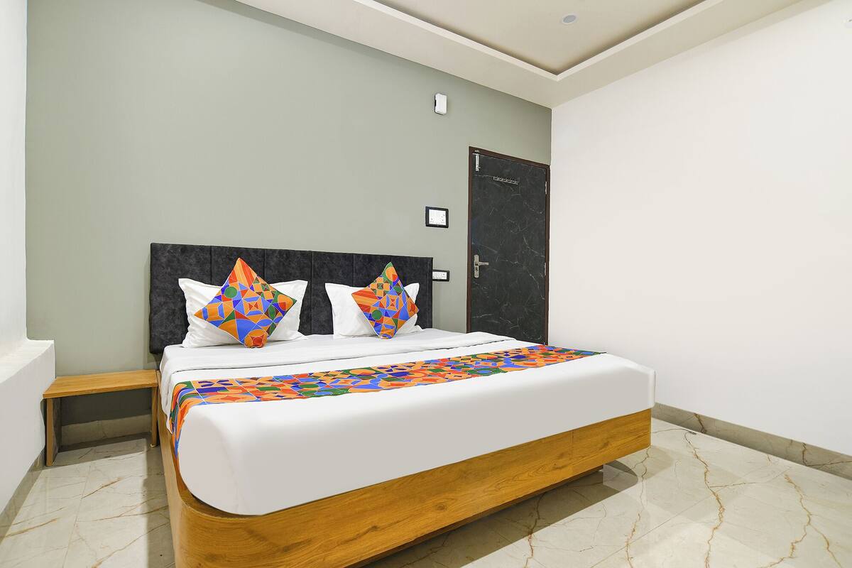 A neatly made bed with a wooden frame and white bedding, a black headboard, and two colorful geometric pillows.