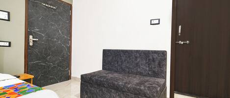 A room with a bed, a small table, a dark-colored chair, a marble floor, and a dark wooden door.