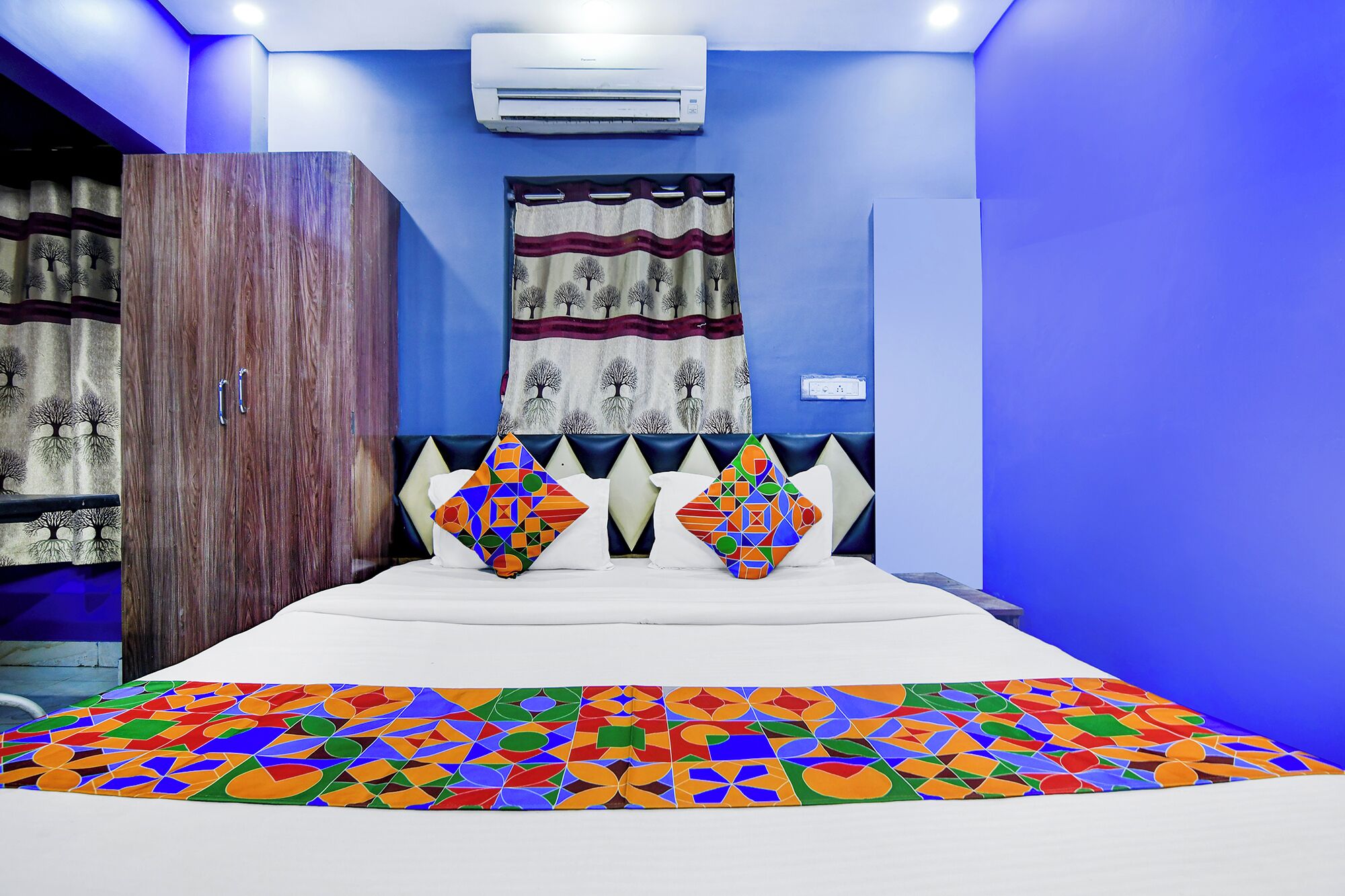 Quarto com cama, guarda-roupa, ar condicionado fixado na parede e cortina com padrão de árvore.