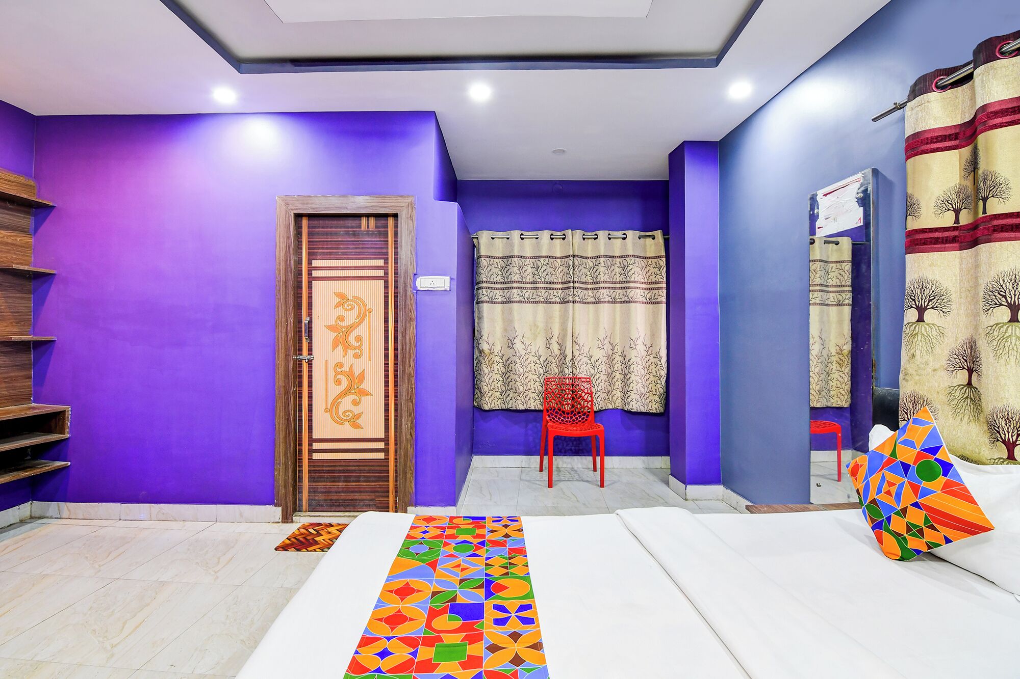 A room with purple walls, a wooden door with a decorative panel, a red chair, a patterned curtain, and a colorful rug.