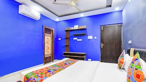 A bedroom with a bed, a ceiling fan, a wall-mounted air conditioner, and a door with a decorative panel. - Fabhotel Love Birds Chinar Park (Barasat)