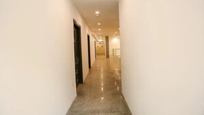 A hallway with a polished floor and white walls, leading to a door at the end. - Fabhotel Sharveen Classic Inn (Gangapur)