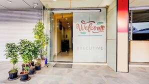A building entrance with a 'Welcome' sign and 'EXECUTIVE' label, potted plants, and a tiled floor. - Fabhotel Chetan Executive (Pune)