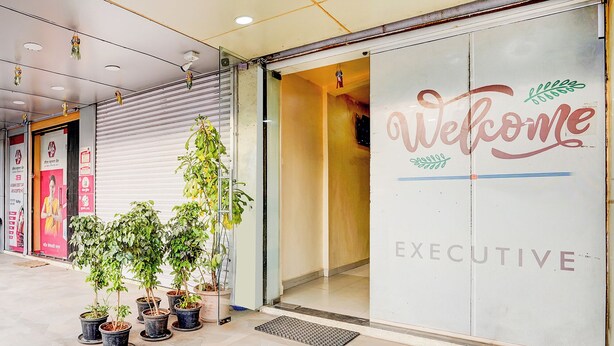 A building entrance with a 'Welcome' sign and a 'EXECUTIVE' label, potted plants, and a closed shutter door. - Fabhotel Chetan Executive (Pune)