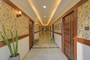 Un pasillo largo y estrecho con papel tapiz estampado, puertas de madera y plantas en macetas.