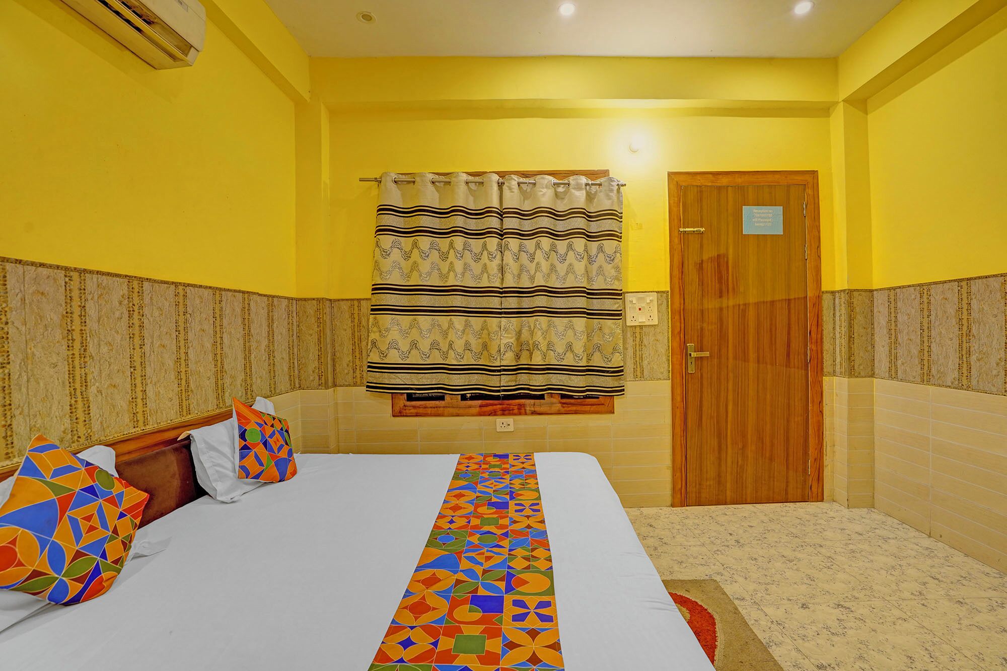 A hotel room with a bed, a patterned bed runner, a wooden door, and a curtain.