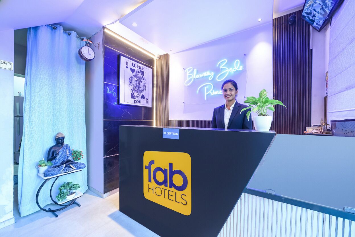 A reception area with a 'fab hotels' sign, a Buddha statue, a clock, and a neon sign that reads 'Blooming Bedz Primez'.