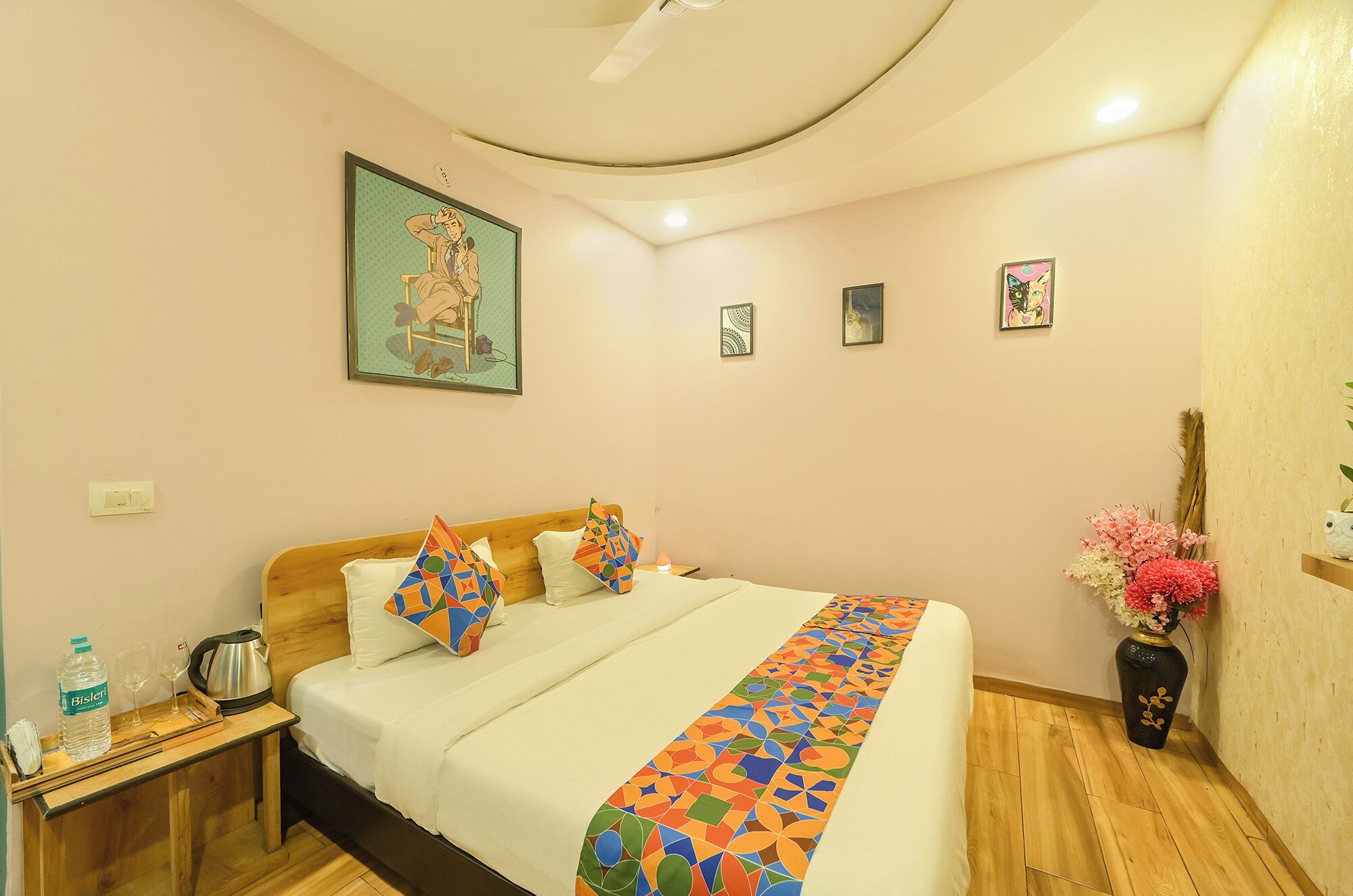 A hotel room with a bed, a nightstand, a vase with flowers, and a painting on the wall.