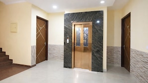 A hallway with a marble wall, a wooden door, and a tiled floor. - Fabhotel Sager Inn (Gurugram)