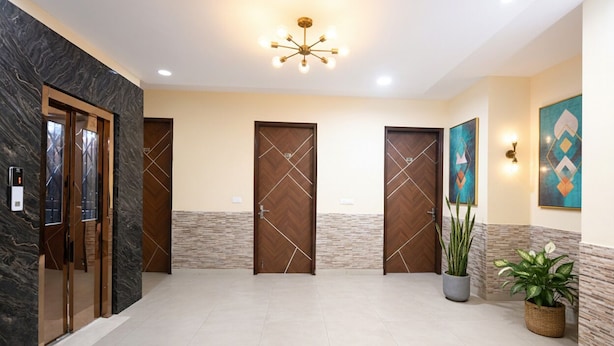 A hotel lobby with marble walls, wooden doors, a modern chandelier, and potted plants. - Fabhotel Sager Inn (Gurugram)