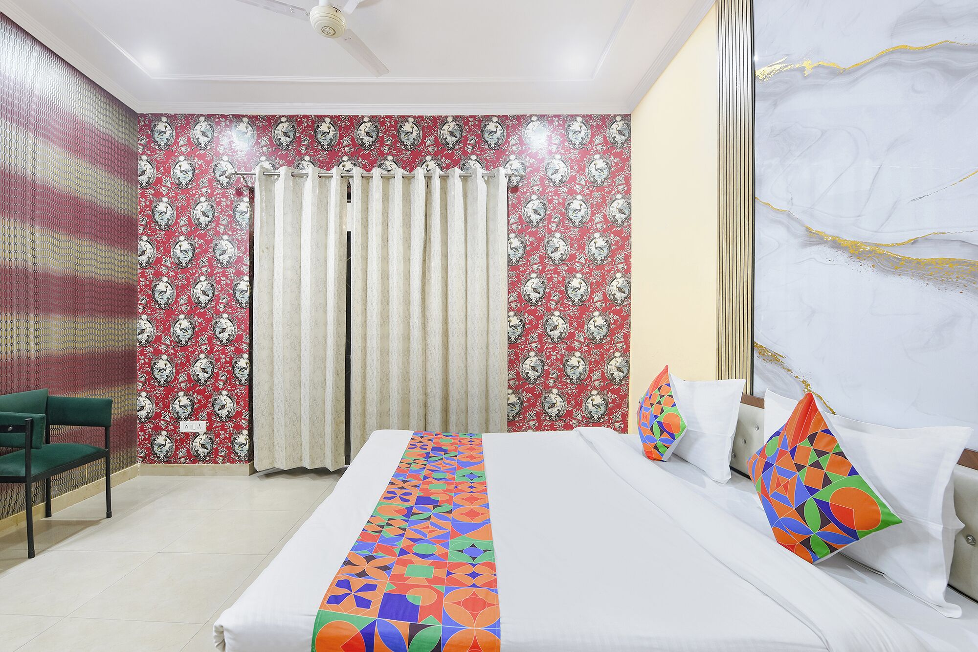 A hotel room with a bed, a chair, a curtain, and a patterned wall.