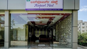 The entrance of the Airport Nest hotel with a glass facade, a reception desk, and a staircase leading inside. - Via Aero Nest (Bengaluru)